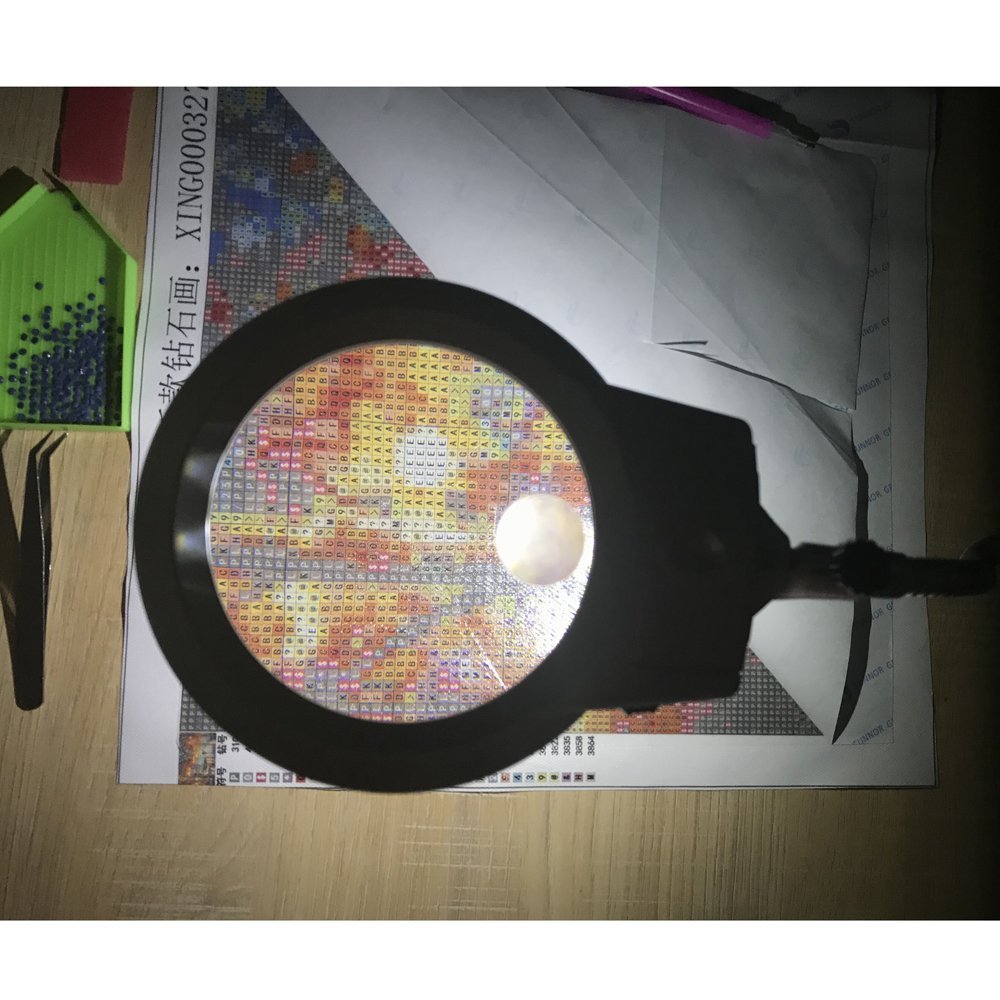 Diamond painting magnifier with clamp over a diamond painting kit, showing tweezers and bead tray.