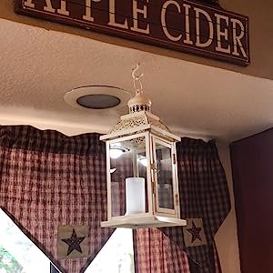 White metal and glass candle lantern hanging from ceiling with decorative curtains and a sign above