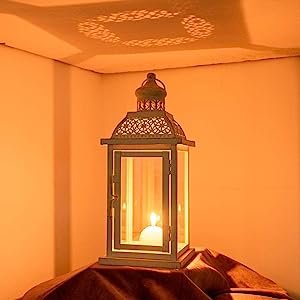 White metal and glass candle lantern with lit candle inside, casting decorative shadows on the ceiling.