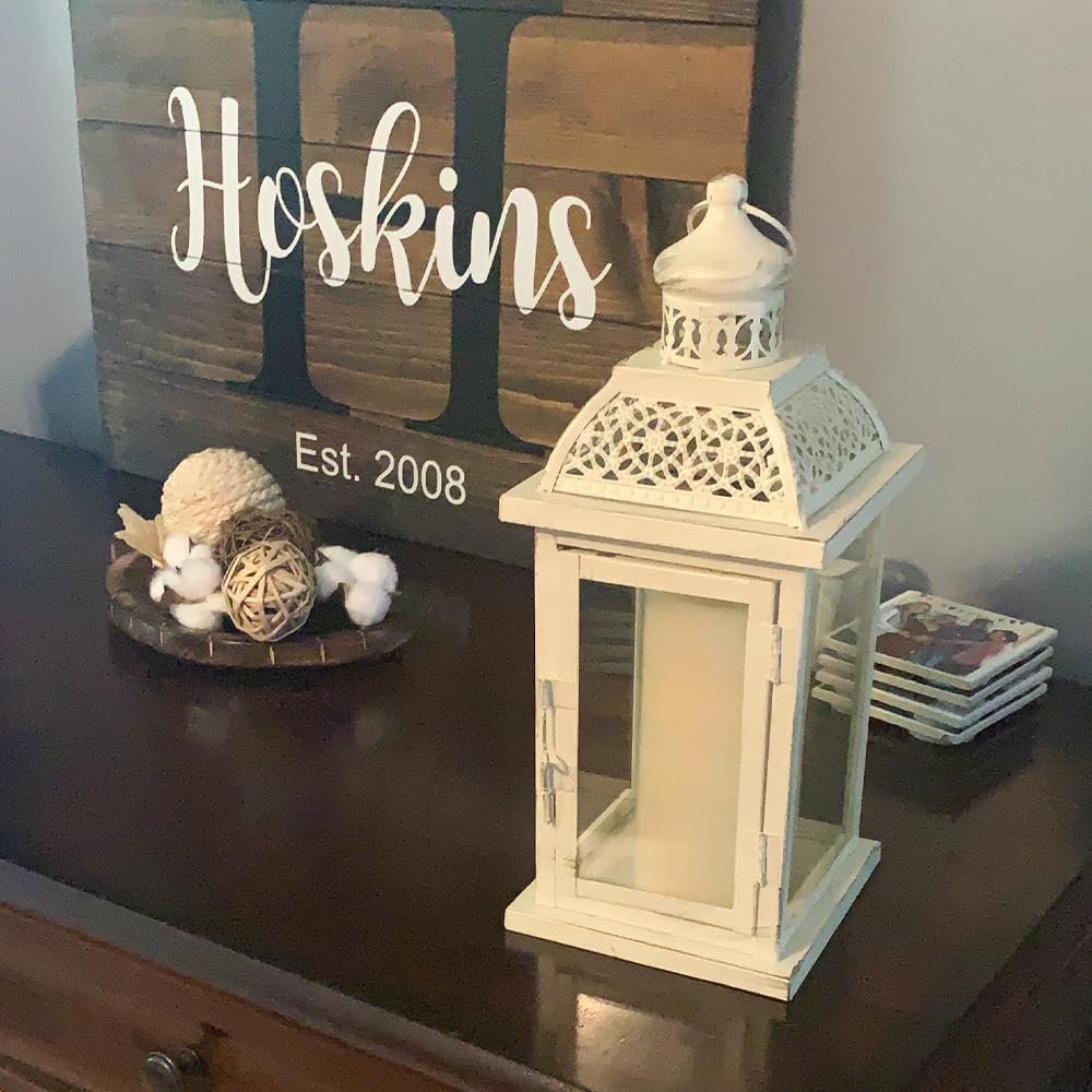 White metal and glass candle lantern on a dark wood surface next to decorative items and a wooden sign.