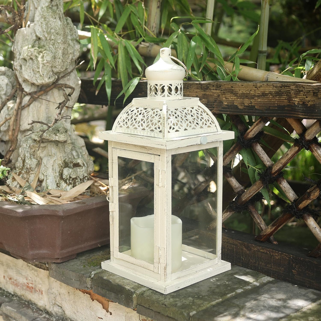 White metal and glass candle lantern with two LED candles inside, set on a stone ledge with bamboo in the background.