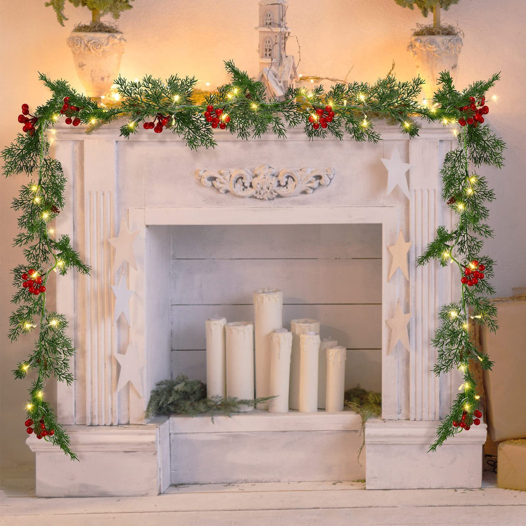 Christmas garland with warm white LEDs, pine needles, red berries draped over a white fireplace mantel with decorative stars and candles.