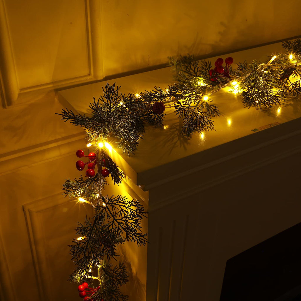 Prelit Christmas garland with warm white LEDs, pine needles, red berries, and pine cones draped over a mantelpiece.