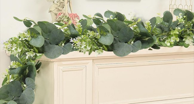 Artificial eucalyptus garland with white blooms draped over a cream-colored cabinet top.