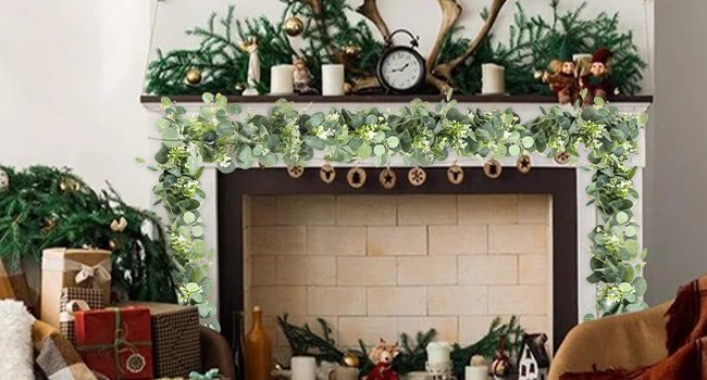 Artificial eucalyptus garland with white blooms draped over a fireplace mantel with Christmas decorations