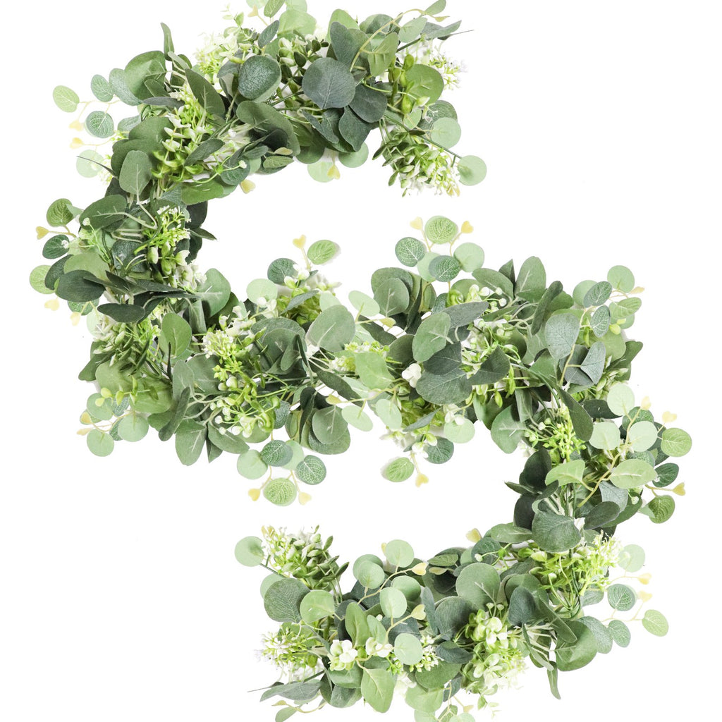 Artificial eucalyptus garland with white blooms on a white background, arranged in a curved shape.