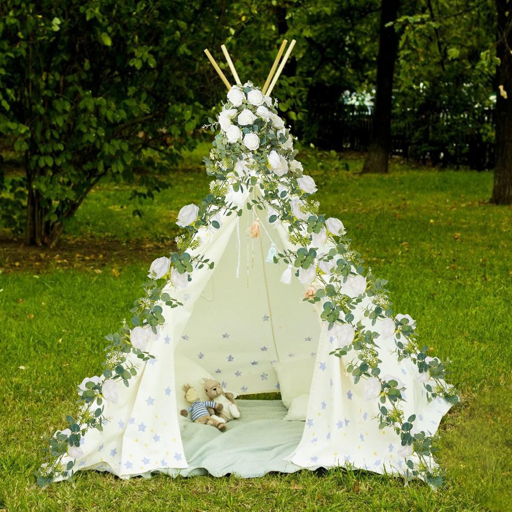 Decorated teepee tent with artificial eucalyptus garland and white blooms in a grassy outdoor setting