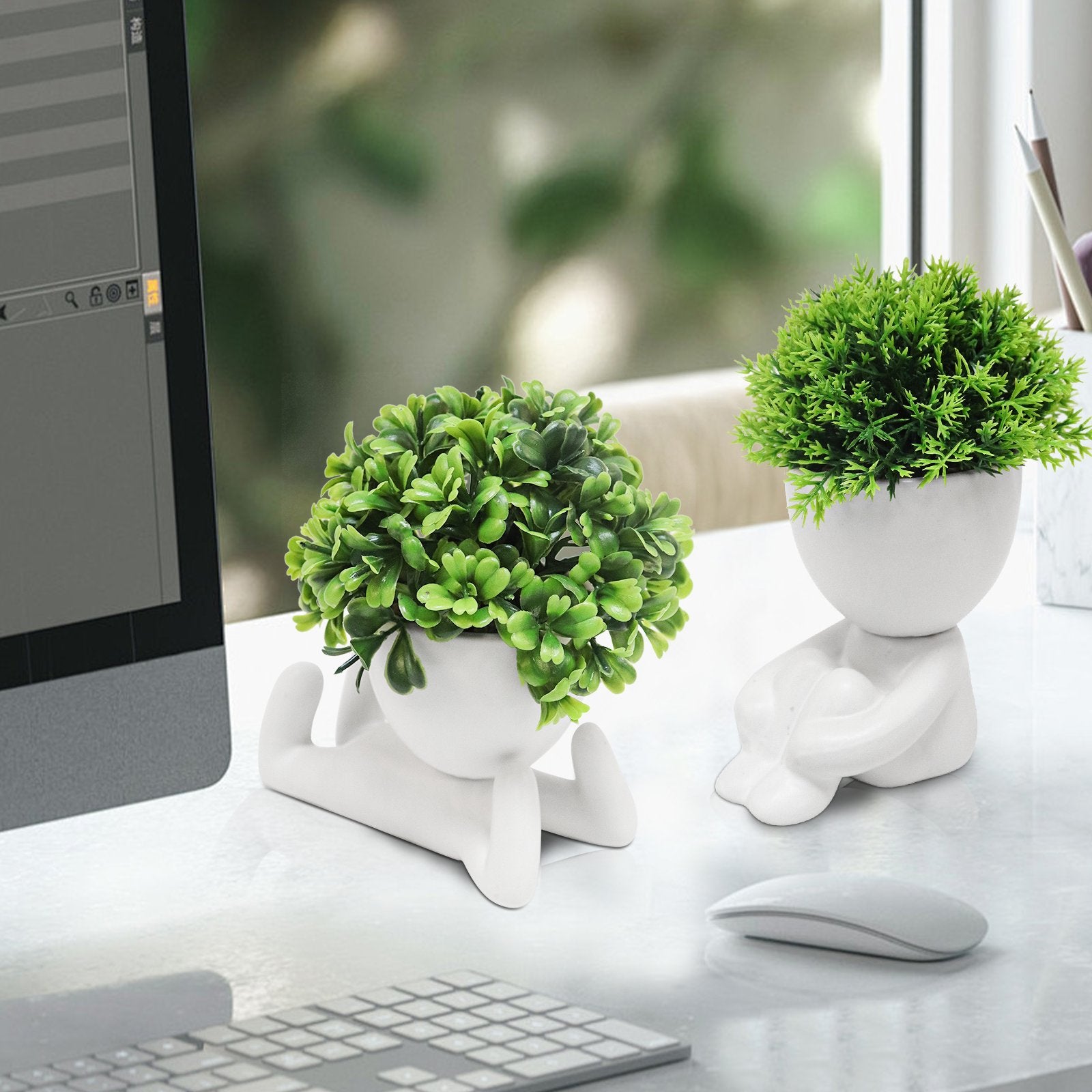 Two white ceramic planters shaped like abstract figures holding green artificial plants on a desk with a computer and keyboard.