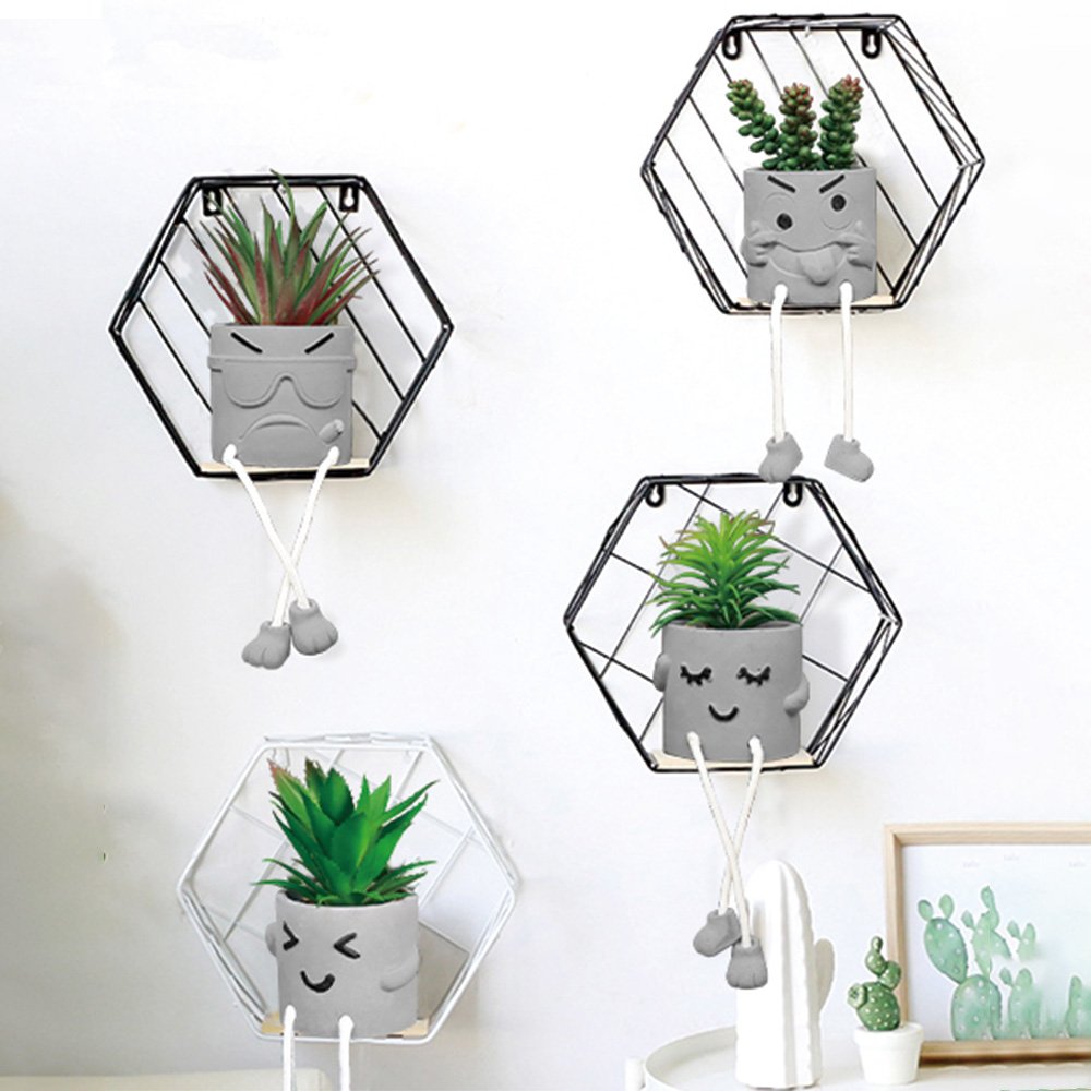 Four decorative planters with artificial succulents on hexagonal shelves, each planter has a face and dangling legs.