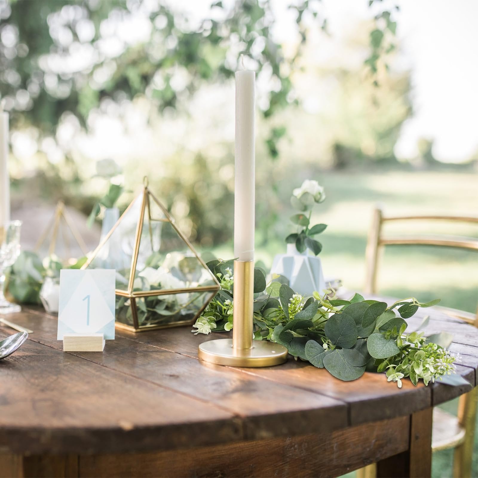 Artificial eucalyptus garland with white blooms on a wooden table with a candle and geometric terrarium