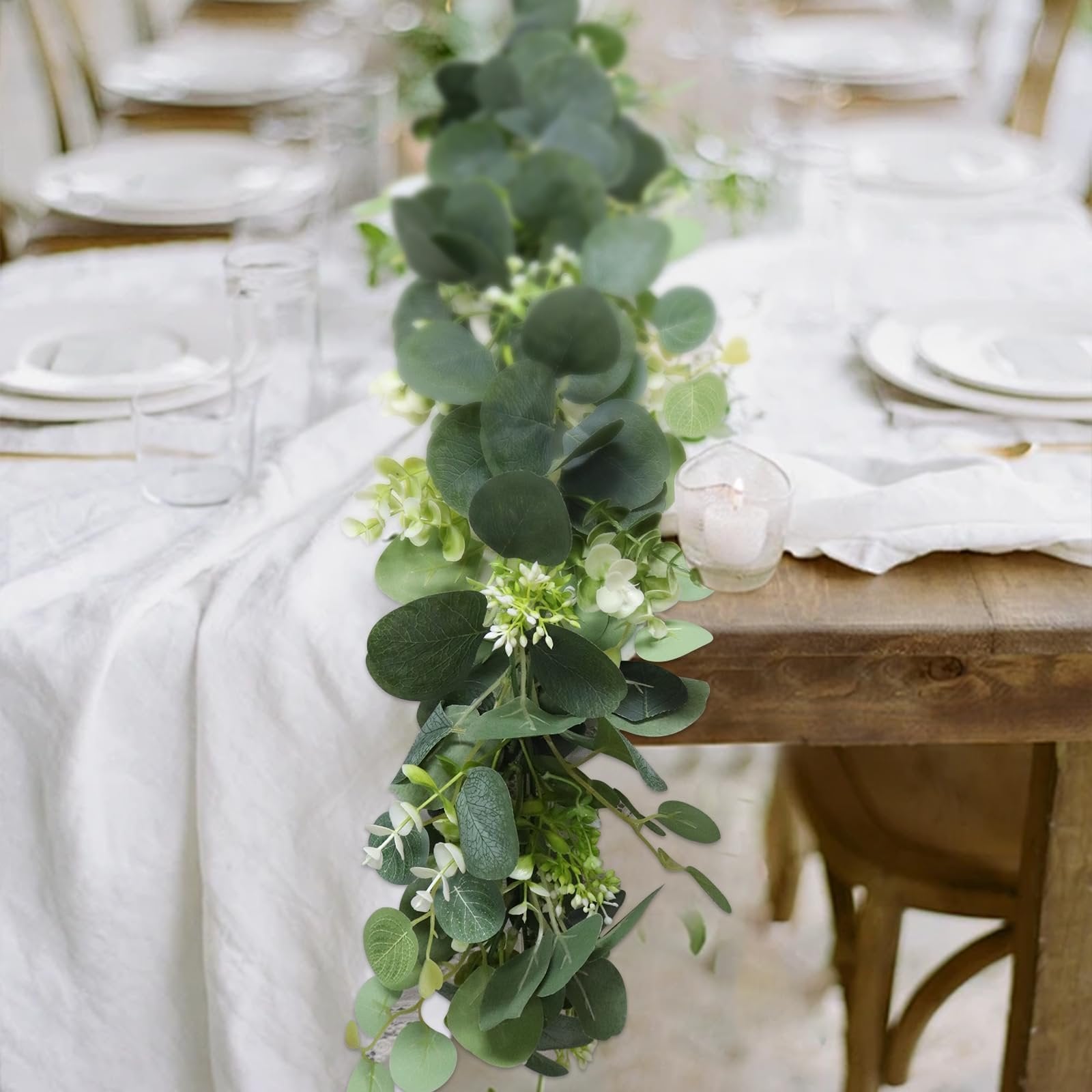 Artificial eucalyptus garland with white blooms draped across a wooden table set for a meal.