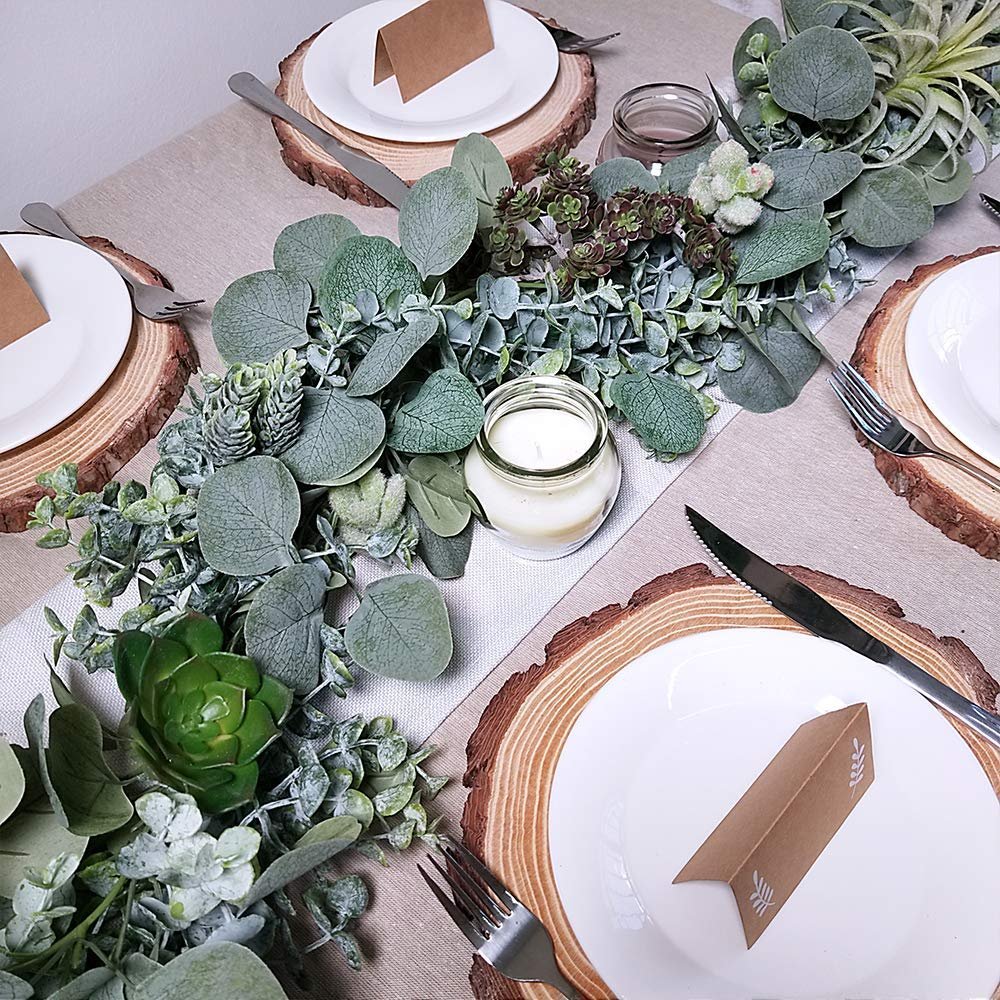 Faux eucalyptus garland with succulents and a candle on a table setting with wood slice chargers