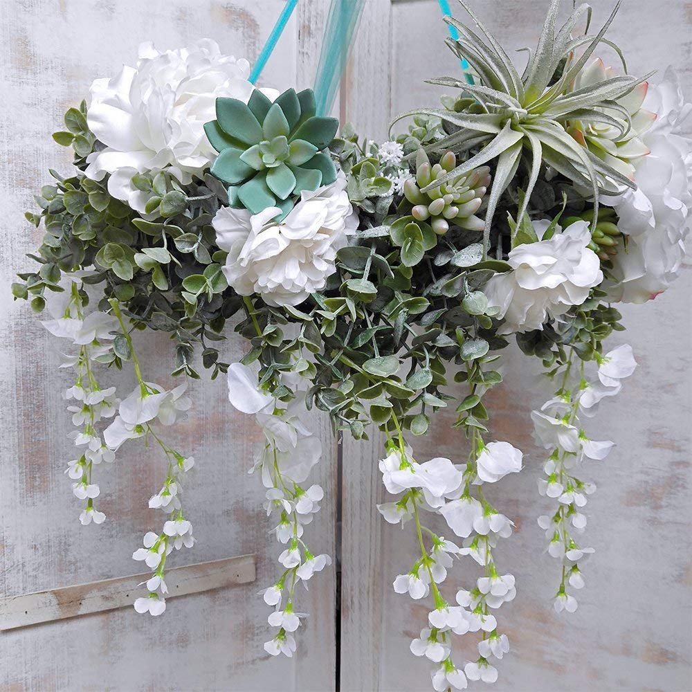 Faux eucalyptus garland with white flowers and succulents hanging against a distressed white wooden background.
