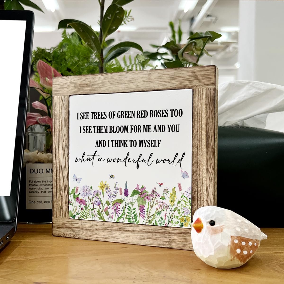 Wooden framed inspirational quote sign with floral border and a small bird figurine on a desk.