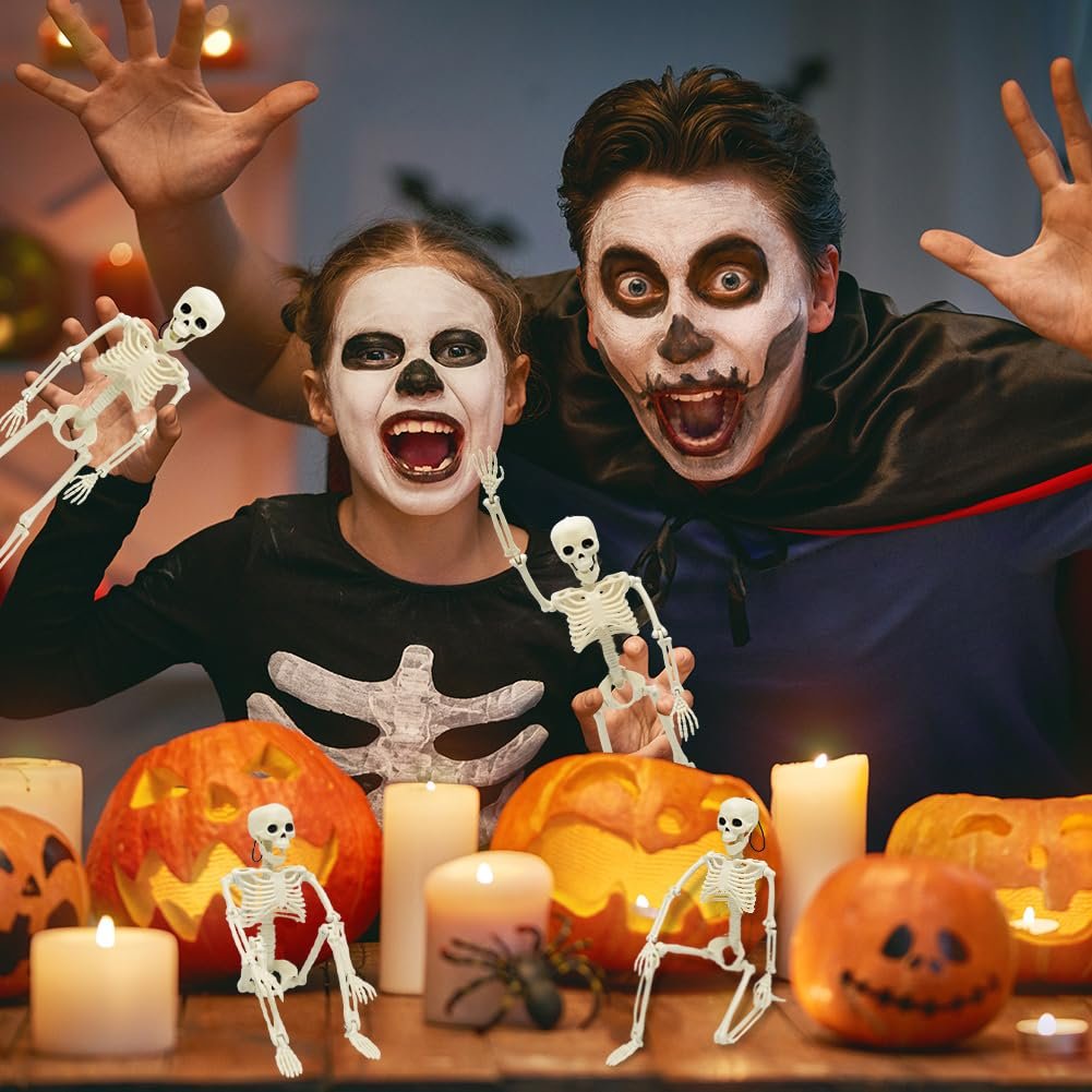 Two people in Halloween costumes holding skeleton figures with carved pumpkins and candles on a table