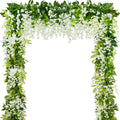 Archway formed by artificial white wisteria garlands with green leaves, isolated on white background.