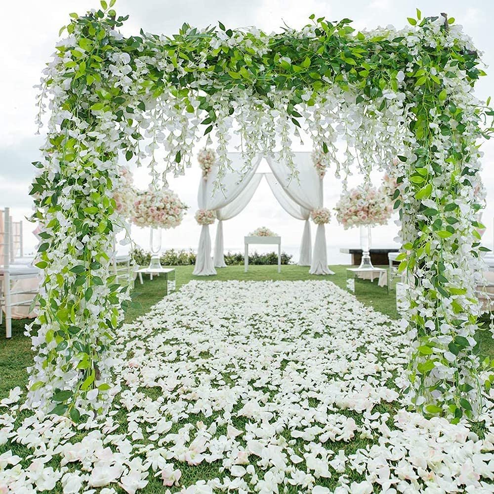 Wedding arch decorated with artificial wisteria garlands and white flower petals covering the ground.
