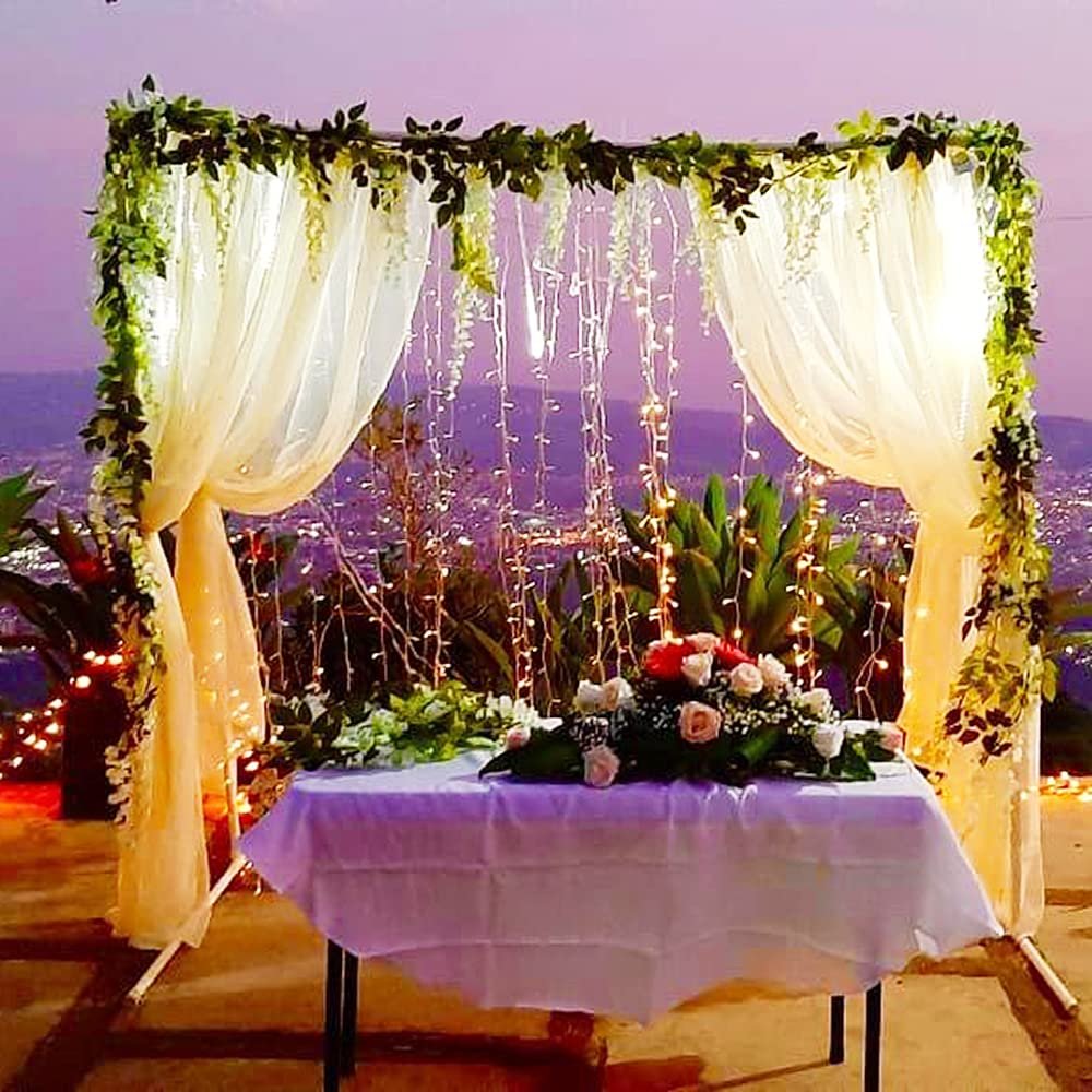Wedding altar with draped curtains, fairy lights, and floral arrangement on a table overlooking a city at dusk