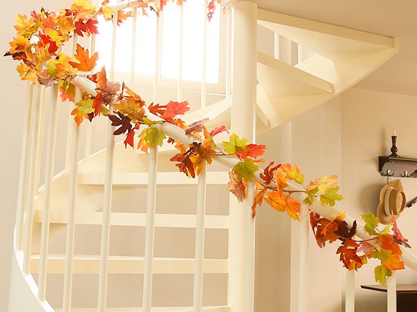 Artificial maple leaf garland draped along a white spiral staircase railing, featuring autumn colors.
