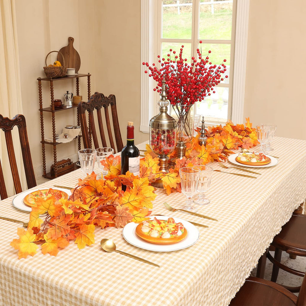 Dining table set for autumn with artificial maple leaf garland, red berry branches, and place settings.