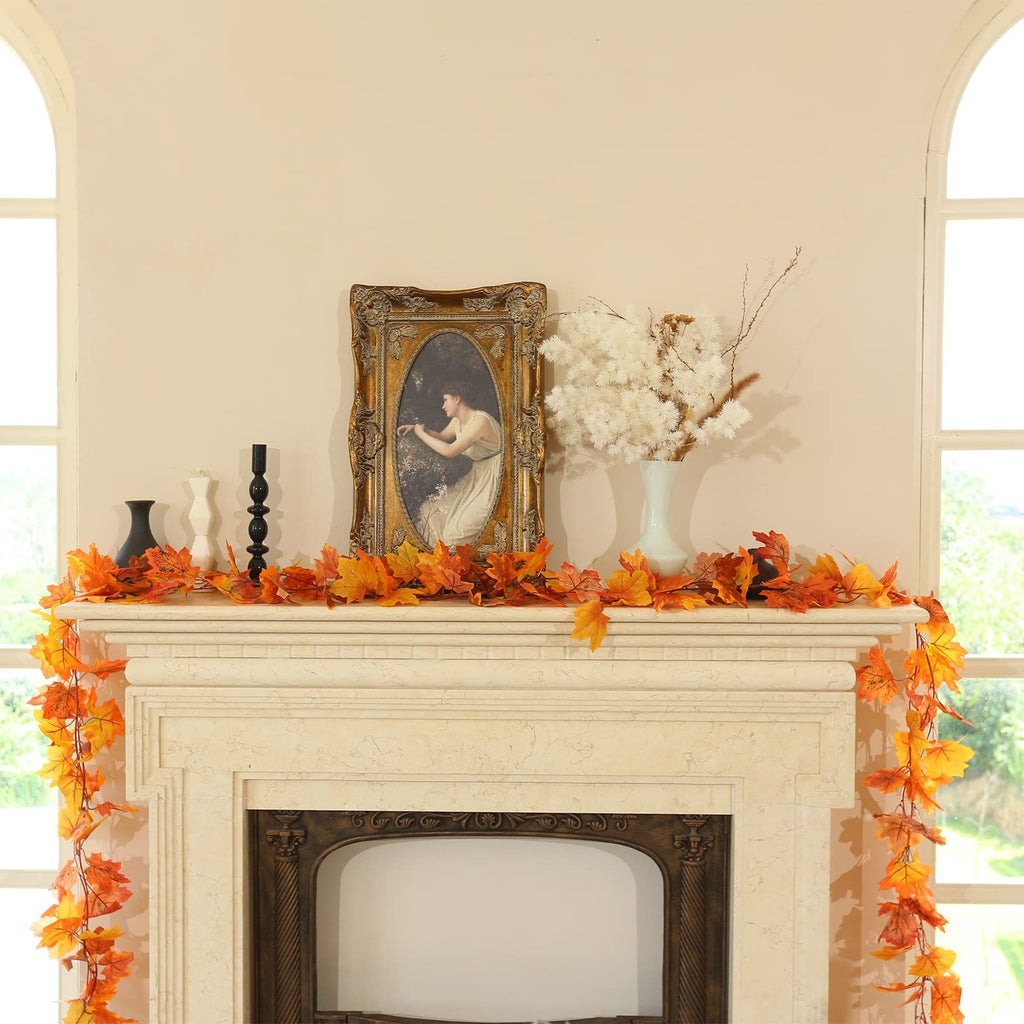Artificial maple leaf garland draped over a fireplace mantel with decorative vases and a framed painting.
