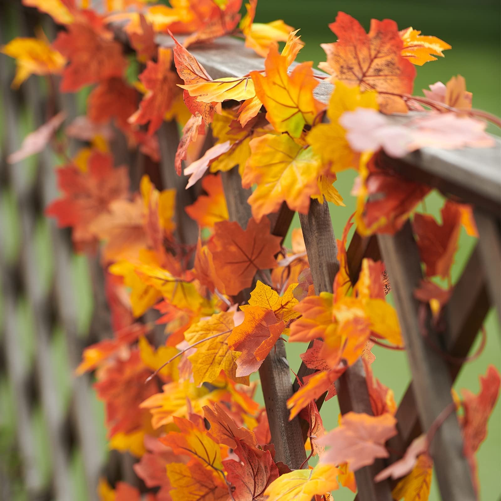 Artificial maple leaf garland in autumn colors draped over a wooden lattice fence