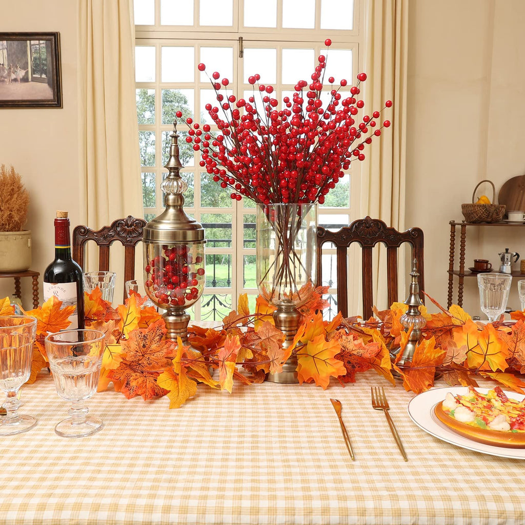 Autumn table setting with artificial maple leaf garland, red berry branches, wine bottle, and place setting.