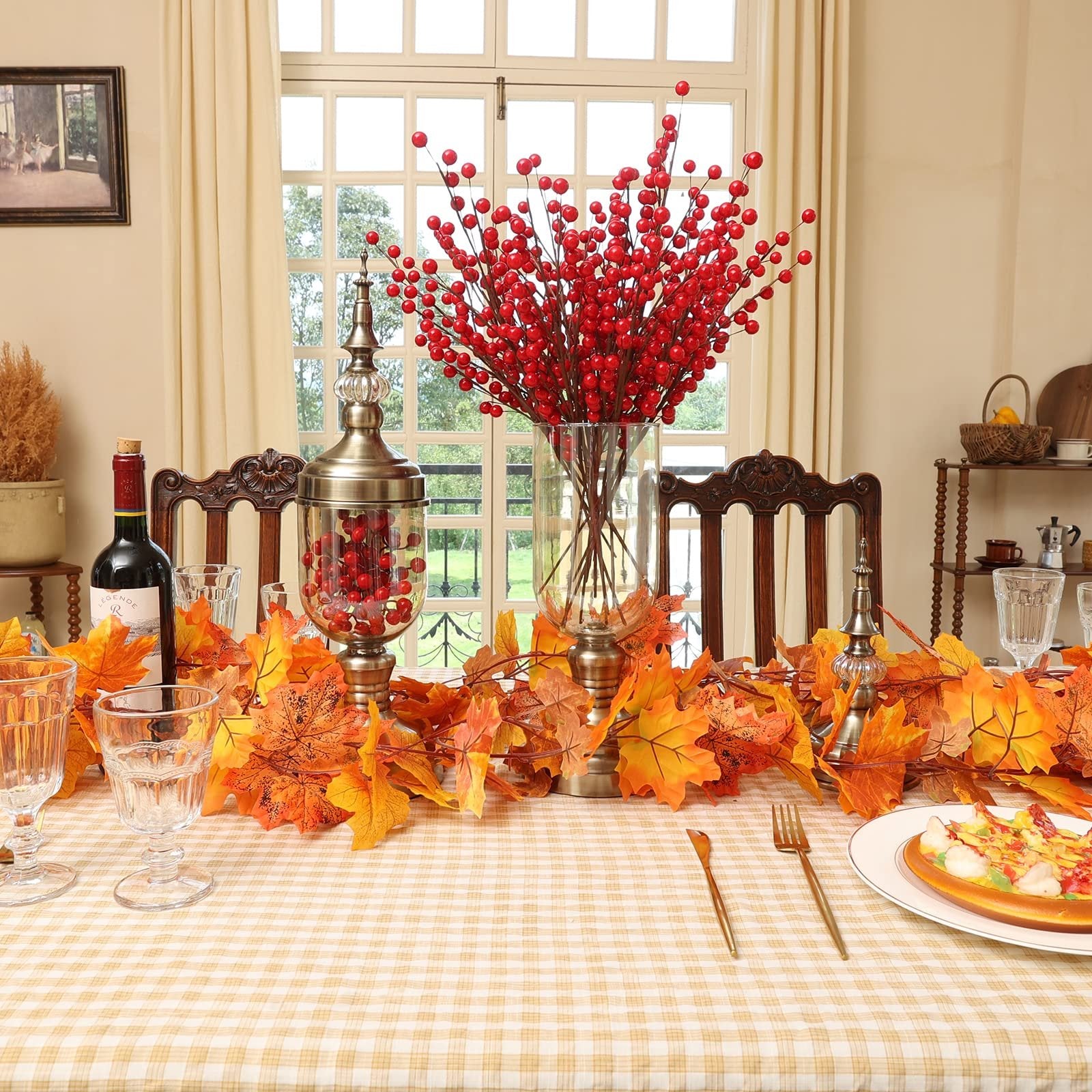 Autumn table setting with artificial maple leaf garland, red berry branches, wine bottle, and place setting.