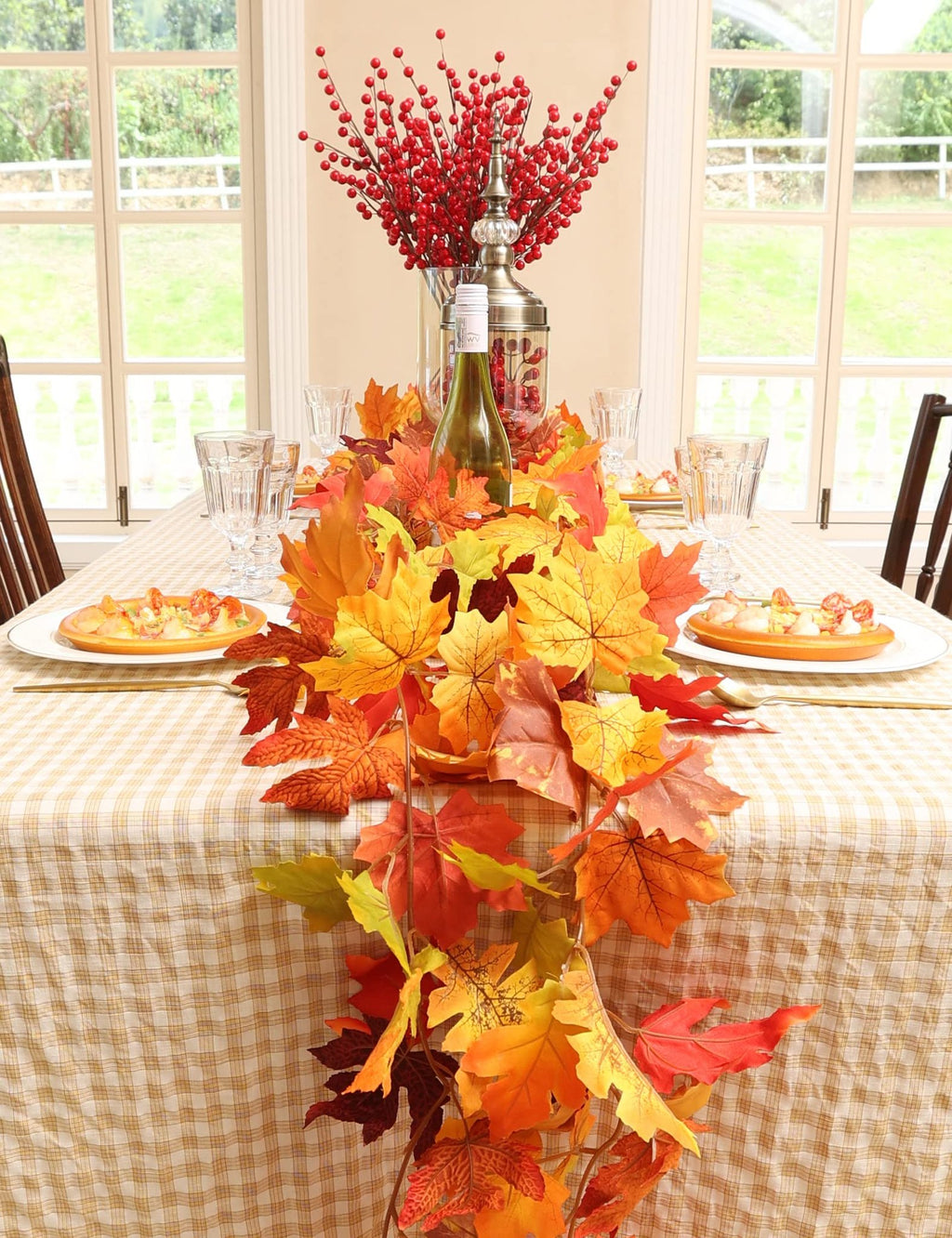 Autumn maple leaf garland draped across a table set for a meal, with glasses, plates, and a centerpiece of red berries.