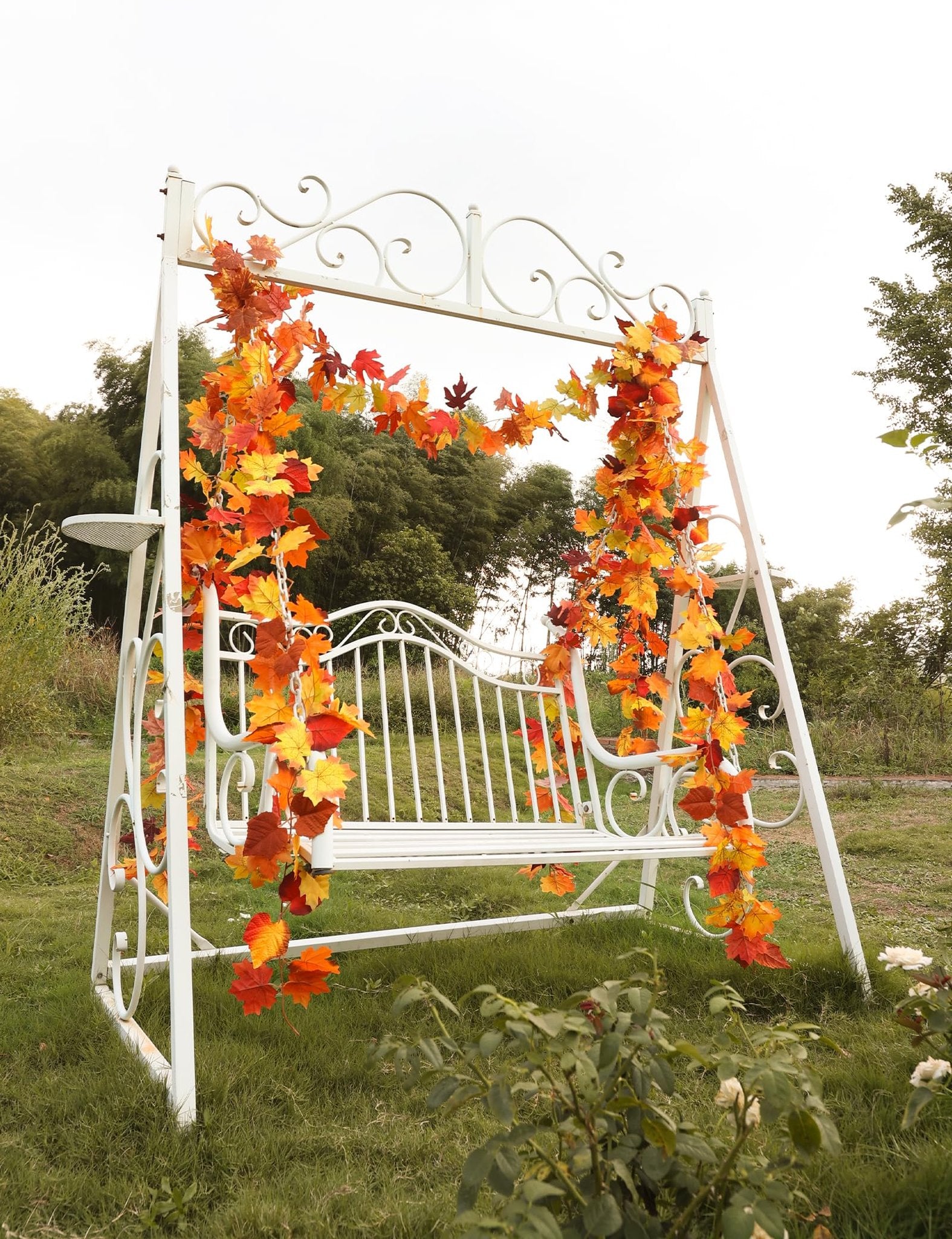 White metal swing decorated with artificial fall maple leaf garland in orange, yellow, and red hues.