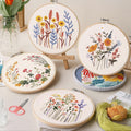 Four embroidery hoops with floral patterns, scissors, and thread on a table