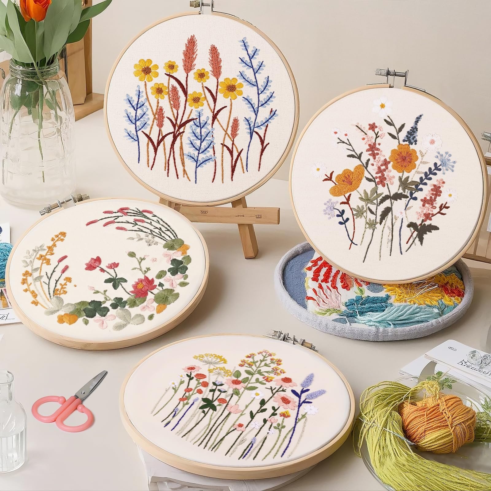 Four embroidery hoops with floral patterns, scissors, and thread on a table
