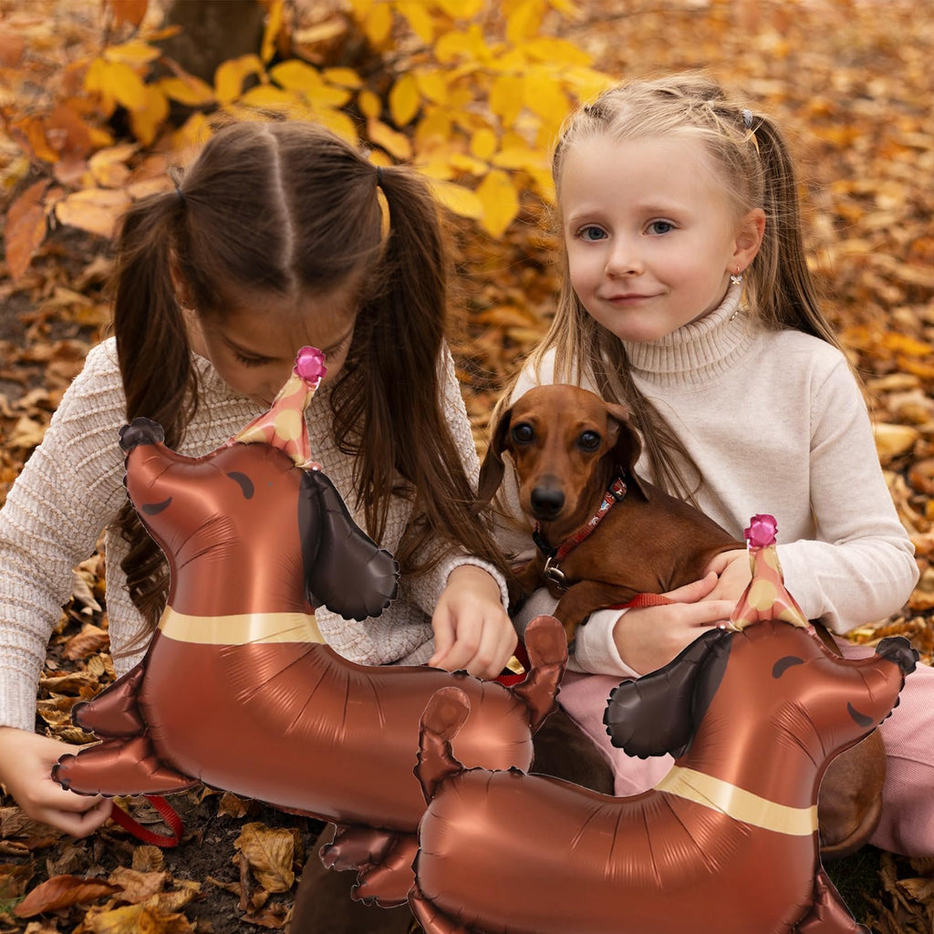 Two girls and a dachshund dog sitting outdoors with dachshund-shaped balloons