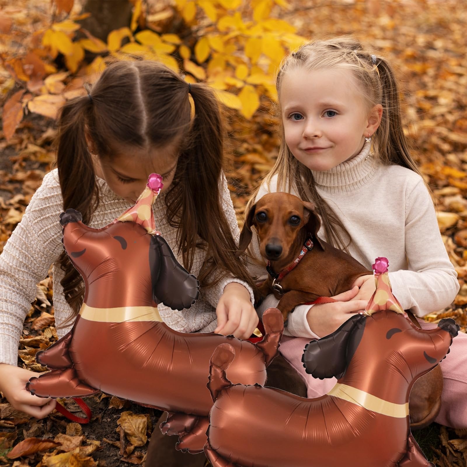 Two girls and a dachshund dog sitting outdoors with dachshund-shaped balloons