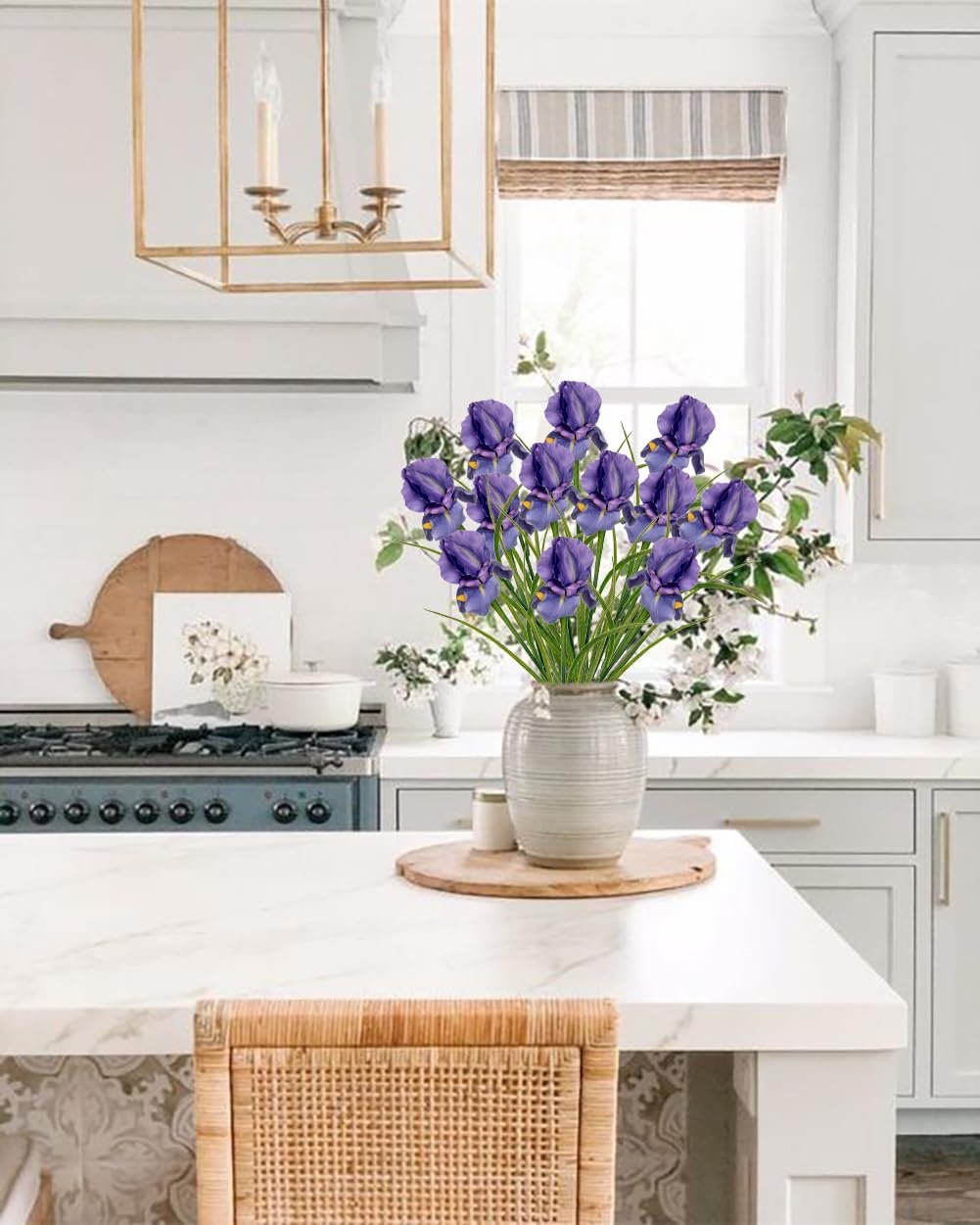 Artificial purple iris flowers in a vase on a kitchen island, with a stove and window in the background.
