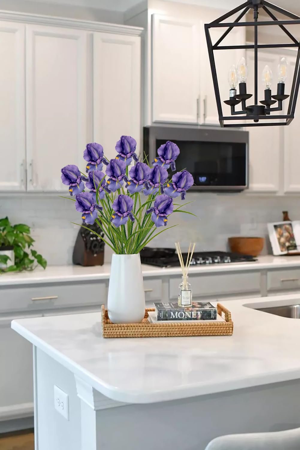 A vase of purple artificial iris flowers sits on a kitchen island with a book and diffuser.