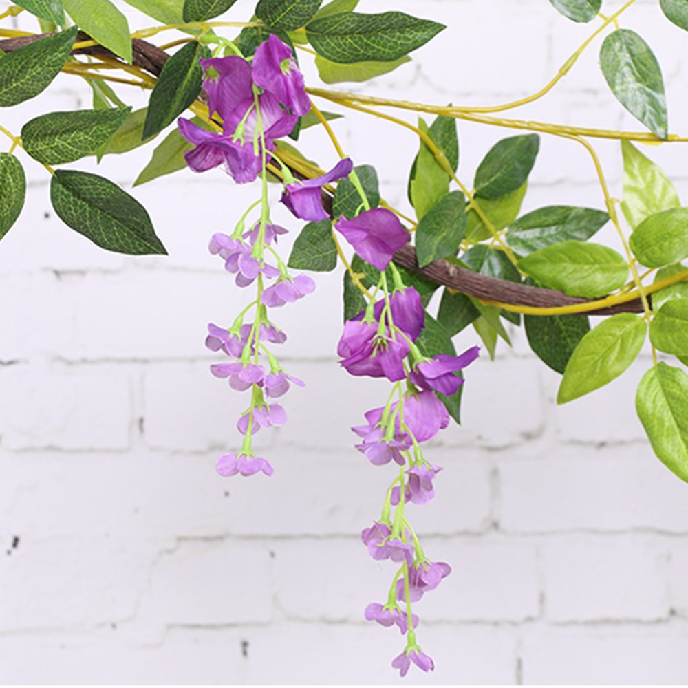 Artificial purple wisteria garland with green leaves hanging against a white brick wall.