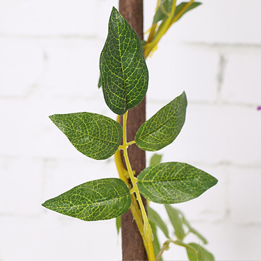 Close-up of artificial wisteria garland stem with green leaves against a white brick background.