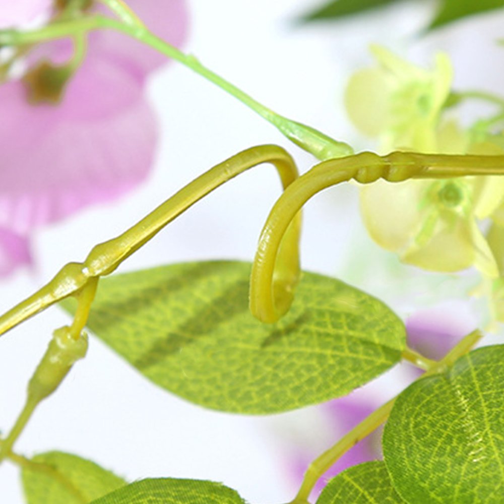 Close-up of artificial purple wisteria garland with green leaves and stems against a white background.