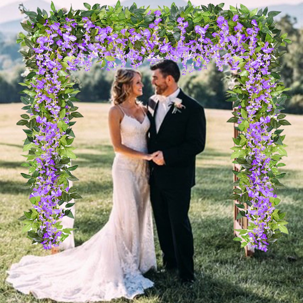 Bride and groom standing under a wedding arch decorated with purple wisteria garlands and green leaves