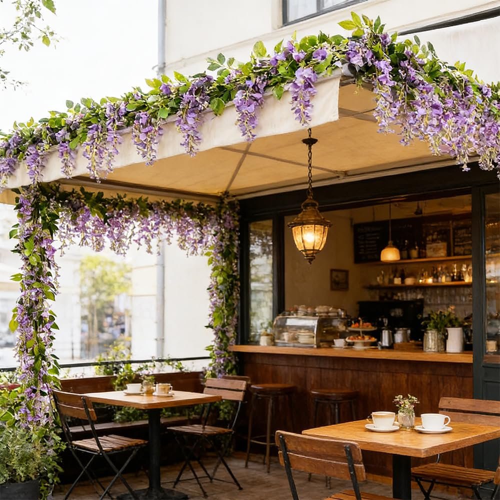 Artificial purple wisteria garlands draped over an outdoor cafe awning and seating area.