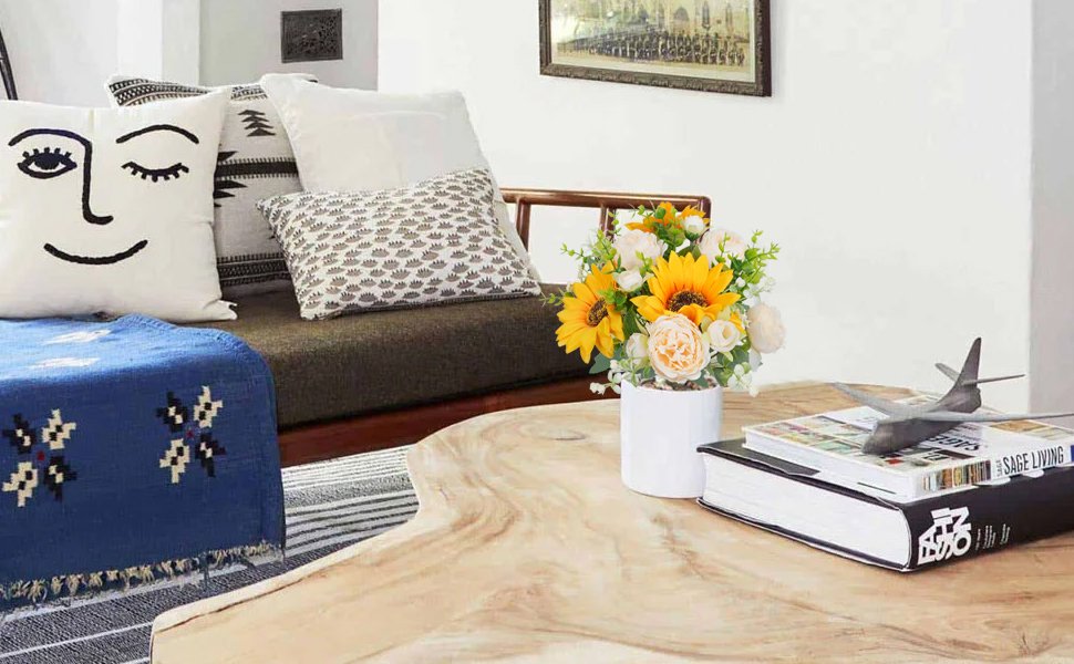 Champagne and yellow silk sunflower and peony bouquet in a white vase on a coffee table with books and an airplane model.