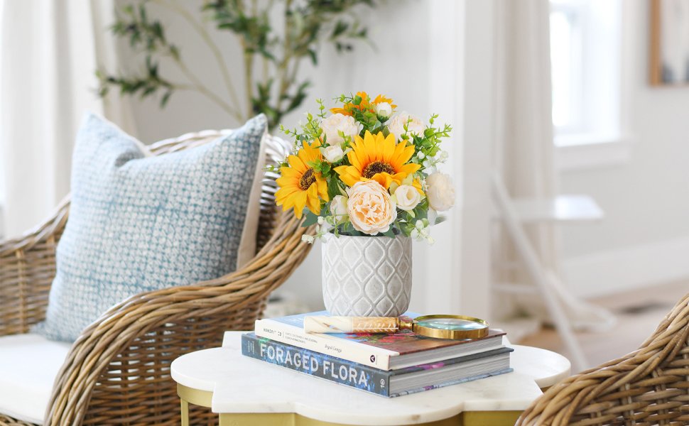 Silk sunflower and peony bouquet in a textured gray vase on top of books, with a magnifying glass.