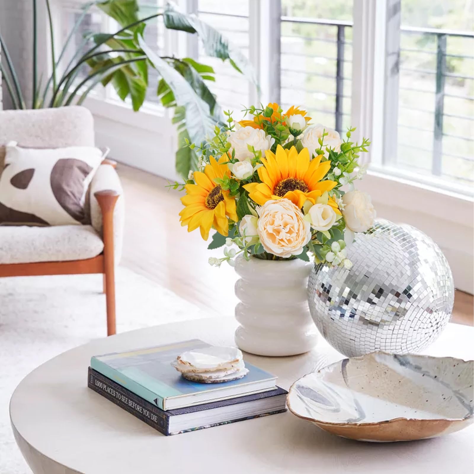 Champagne and yellow silk sunflower and peony bouquet in a white vase on a coffee table with books and a disco ball.