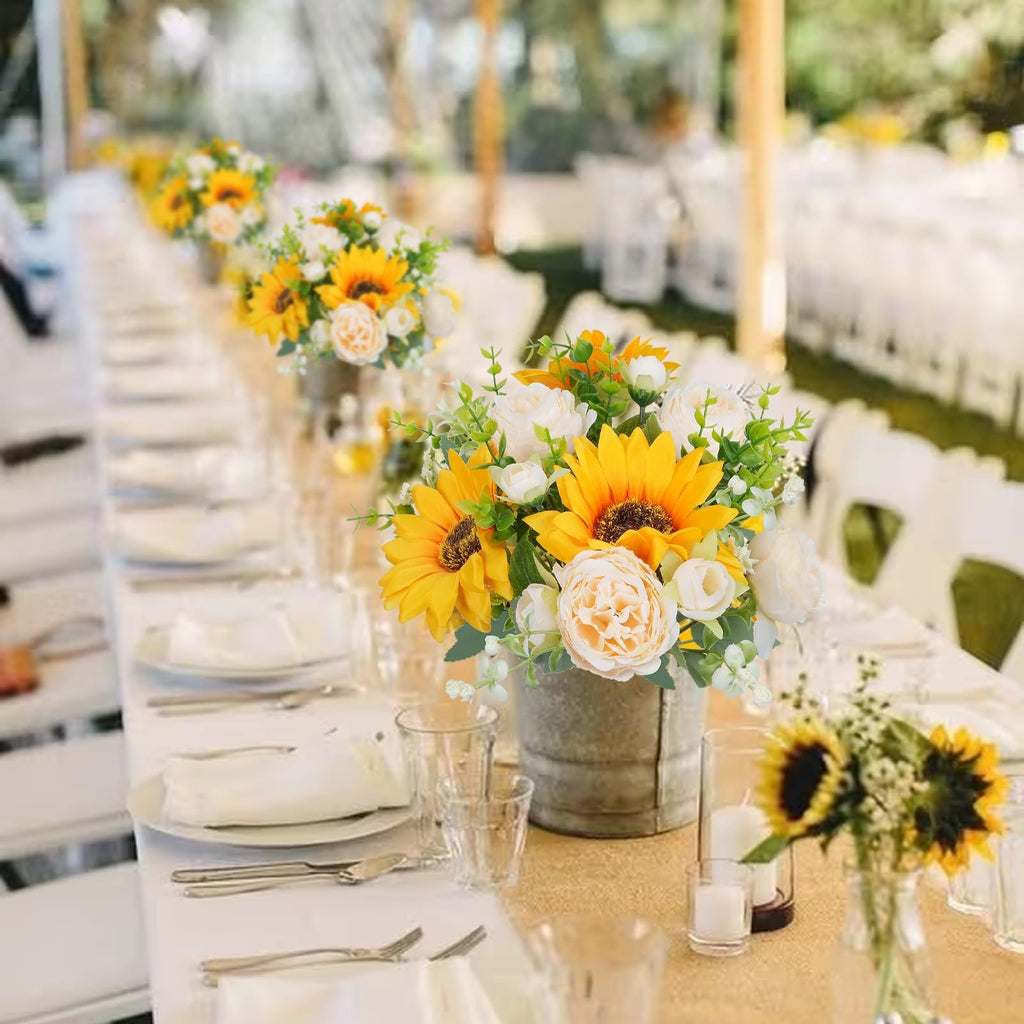 Silk sunflower and peony bouquets in galvanized buckets on a long table setting at an outdoor event.