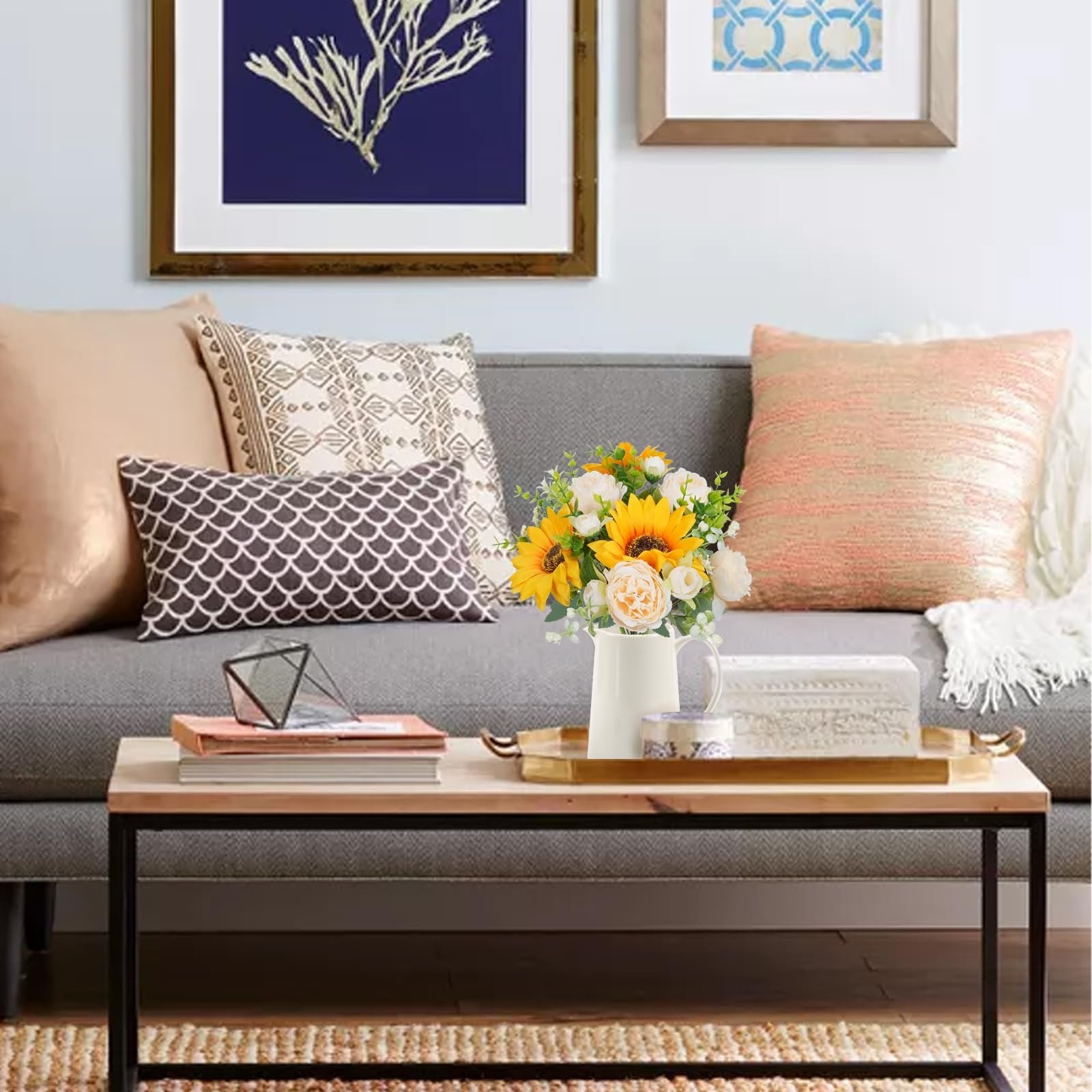 Silk sunflower and peony bouquet in a white pitcher on a coffee table with decorative pillows on a sofa.