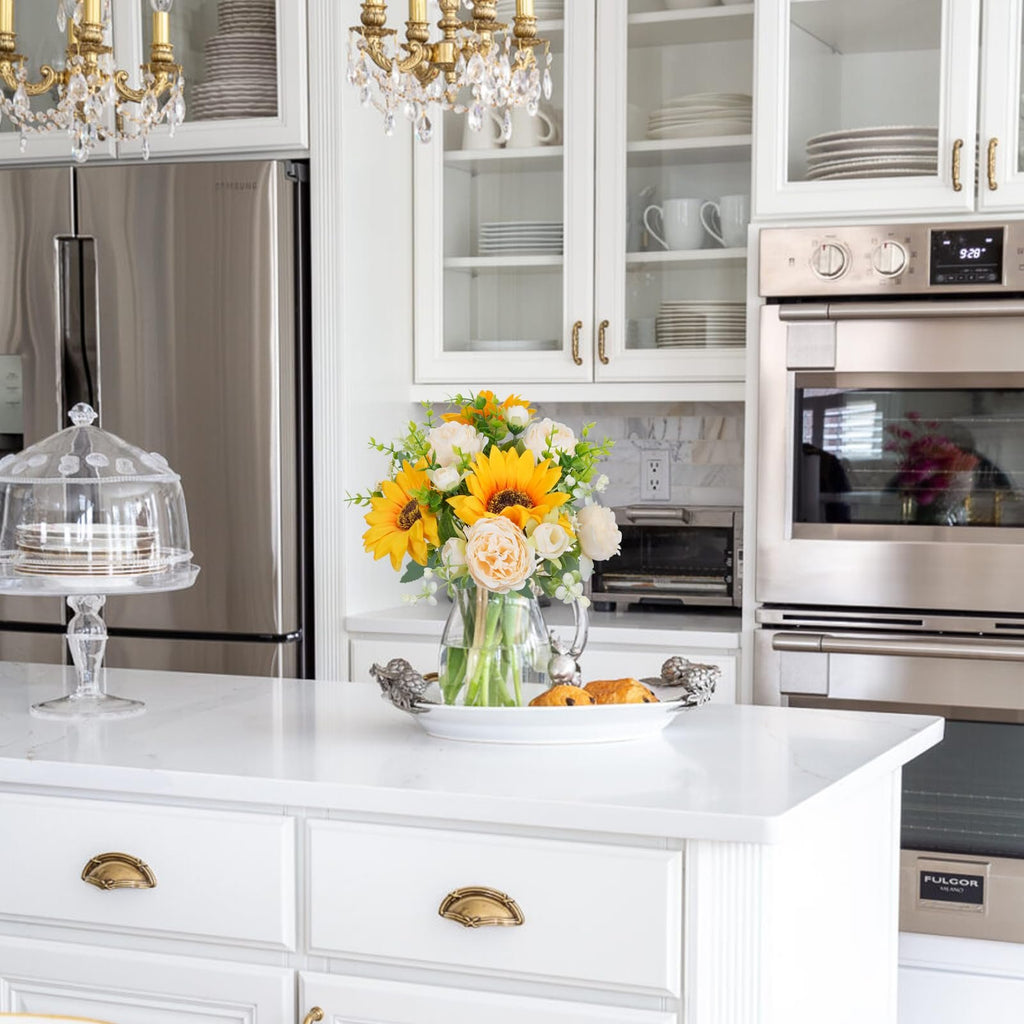 Silk sunflower and peony bouquet in a glass vase on a kitchen island with pastries