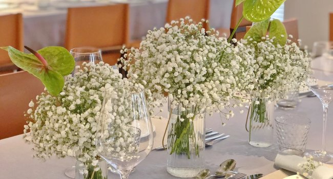 Three vases of white artificial baby's breath flowers with green anthurium accents on a table setting.