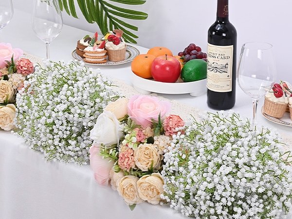 Artificial baby's breath flowers arranged on a table with cupcakes, fruit, and wine.