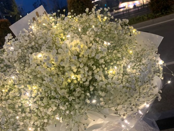 Close-up of a bouquet of white artificial baby's breath flowers with integrated fairy lights, wrapped in white paper.